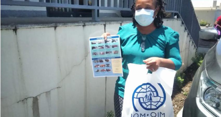 Woman wearing surgical mask holds information poster on COVID-19 and IOM donation bag