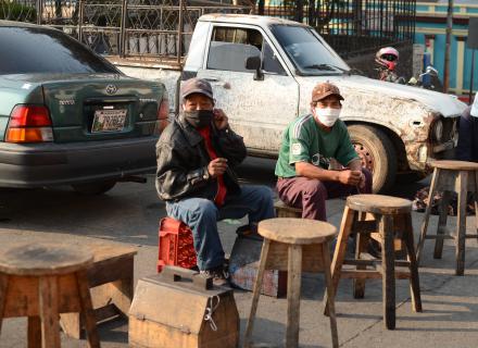 Dos hombres mayores con máscaras de protección ofrecen limpieza de zapatos en una ciudad centroamericana
